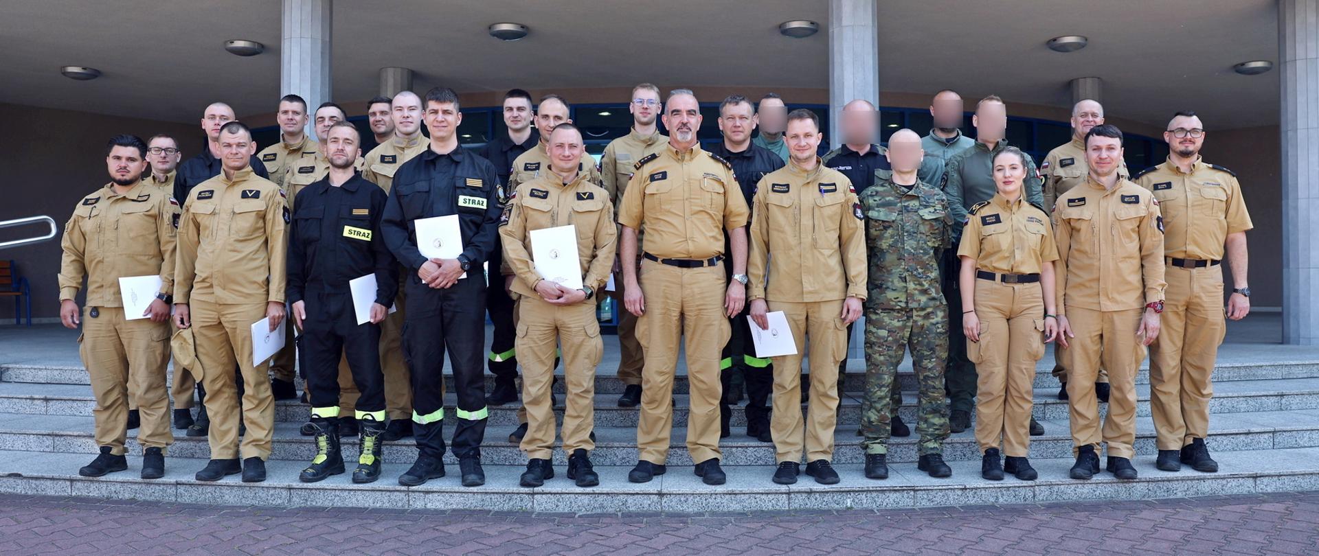 Pamiątkowe zdjęcie grupowe funkcjonariuszy PSP oraz Straży Granicznej (20 osób) w towarzystwie Zastępcy Komendanta Centralnej Szkoły PSP oraz funkcjonariuszki i czterech funkcjonariuszy CS PSP