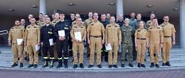 Pamiątkowe zdjęcie grupowe funkcjonariuszy PSP oraz Straży Granicznej (20 osób) w towarzystwie Zastępcy Komendanta Centralnej Szkoły PSP oraz funkcjonariuszki i czterech funkcjonariuszy CS PSP
