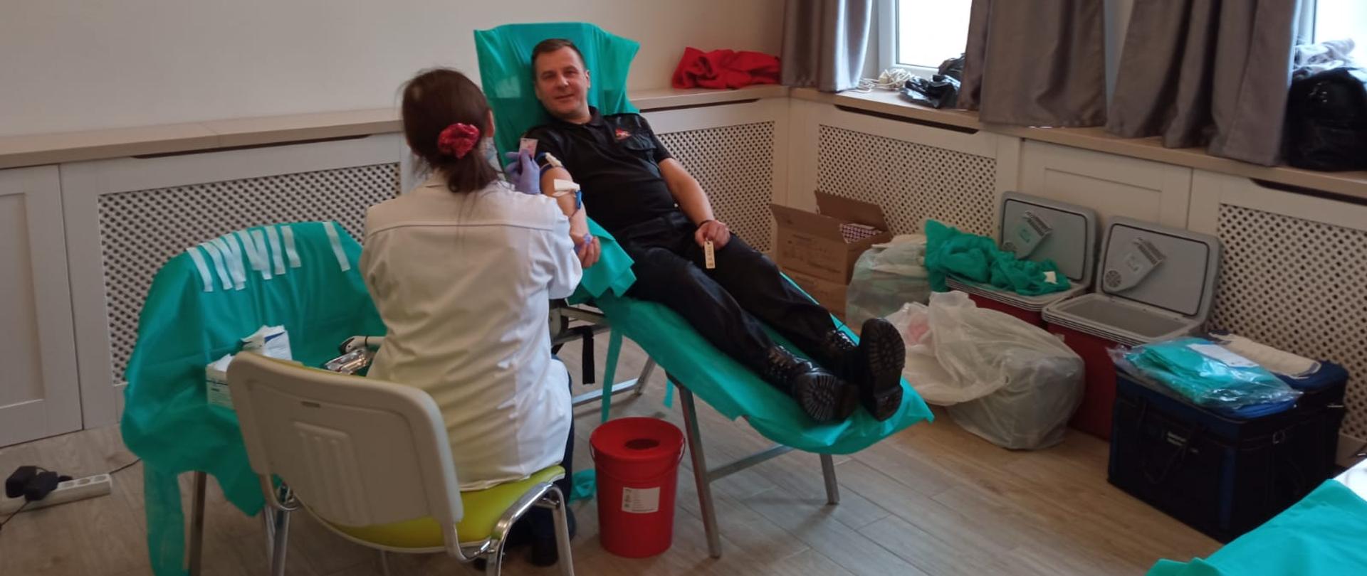 Zdjęcie przedstawia funkcjonariusza Komendy Powiatowej Państwowej Straży Pożarnej mł. bryg. Andrzeja Jabłońskiego, podczas oddawania krwi na rzecz Pani Anny Czarneckiej