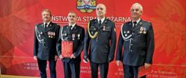 Na zdjęciu Komendant Miejski Państwowej Straży Pożarnej w Sosnowcu w umundurowaniu galowym oraz strażacy OSP w umundurowaniu galowym. W tle widoczne logo Państwowej Straży Pożarnej na czerwonym tle.