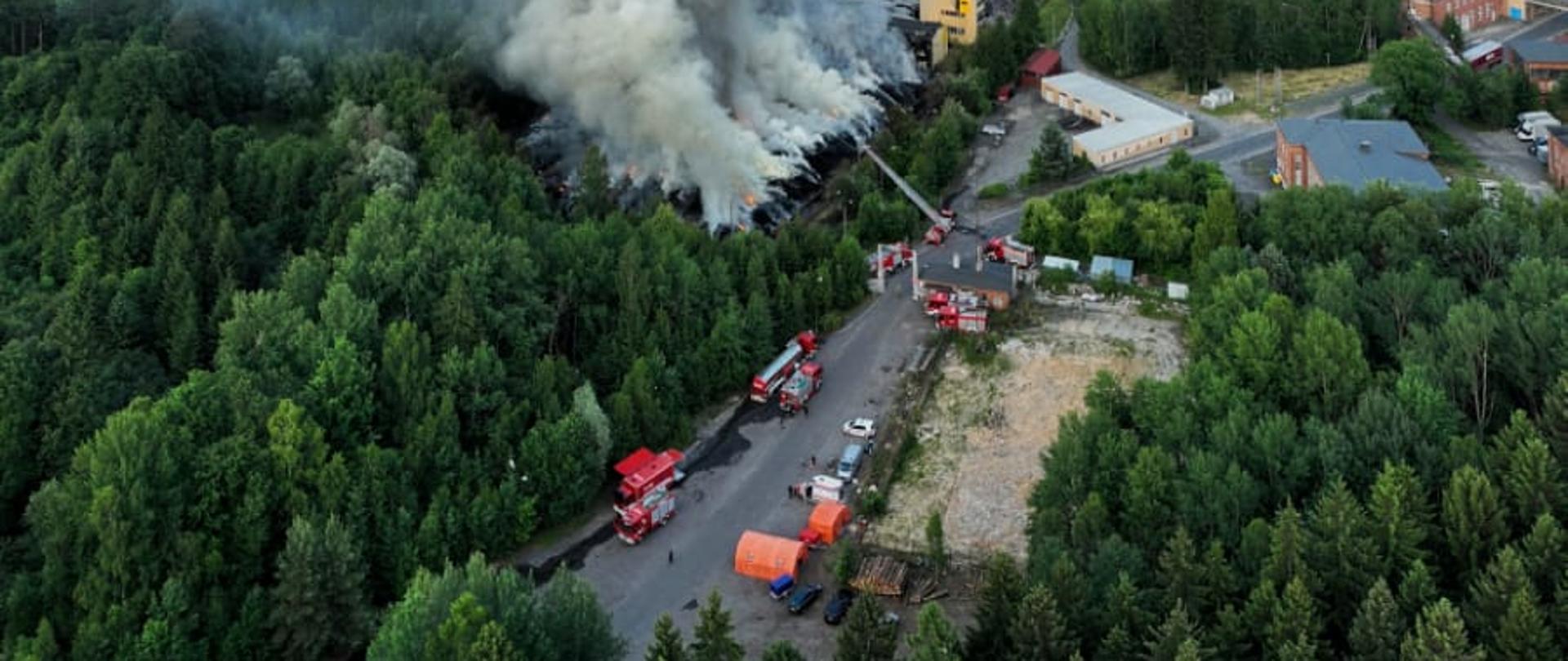 unoszący się dym nad zakładem produkcyjnym w związku z pożarem (ujęcie z samolotu) widoczne pojazdy gaśnicze
