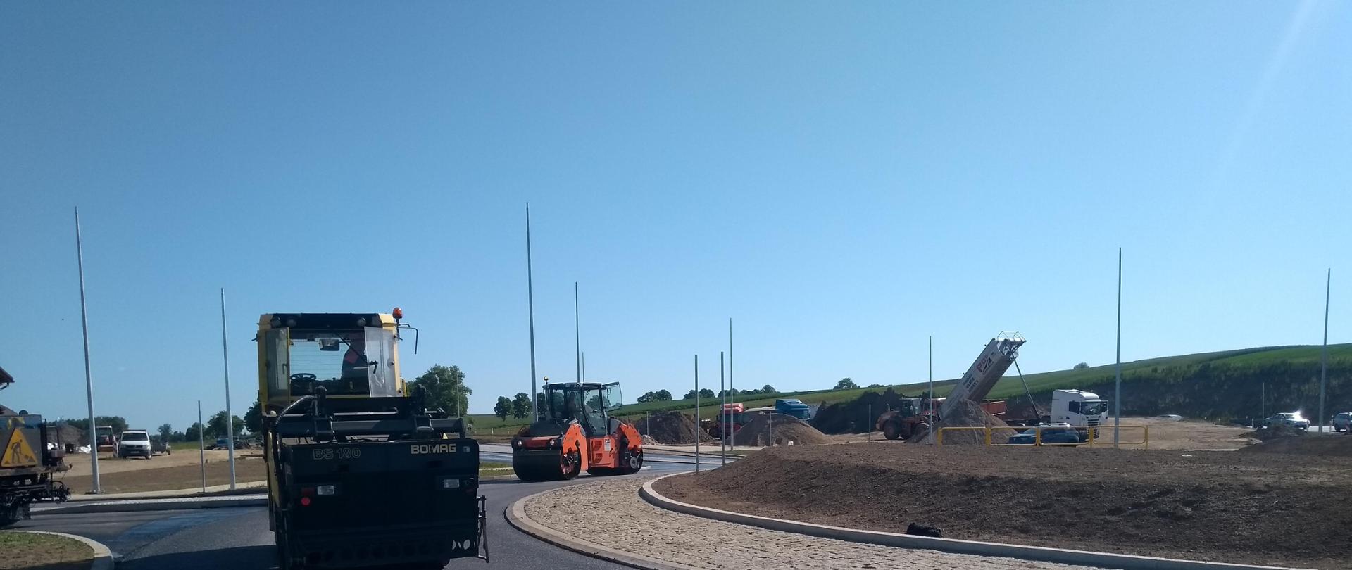 Dwa walce gładzą nawierzchnię asfaltu na budowie ronda. W oddali widać ciężarówkę z uniesioną naczepą