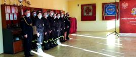 Strażacy w dwuszeregu podczas uroczystej zbiórki. Pierwszy od lewej strażak w mundurze wyjściowym, następnie część pododdziału w umundurowaniu koszarowym. Dwoje ostatnich funkcjonariuszy w umundurowaniu wyjściowym.
