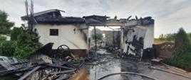 Na zdjęciu widoczny spalony budynek konstrukcji murowanej. Budynek pozbawiony dachu, spalone elementy konstrukcyjne złożone przez obiektem. Widać fragment wypalonego wnętrza budynku.