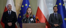 Na zdjęciu minister Katarzyna Pełczyńska-Nałęcz przy mównicy w otoczeniu uczestników spotkania. W tle flaga Polski i UE