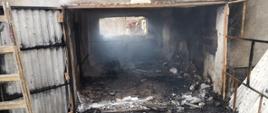 Na zdjęciu spalone pomieszczenie budynku gospodarczego. W tle dwóch strażaków.