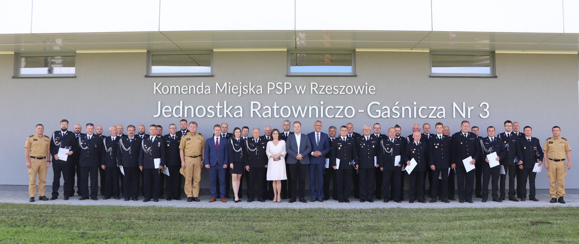 Zdjęcie przedstawia pamiątkową fotografię przedstawicieli druhów OSP, którzy otrzymali dofinansowanie oraz przybyłych gości. W tle widoczna jest Jednostka Ratowniczo-Gaśnicza Nr 3 w Rzeszowie.