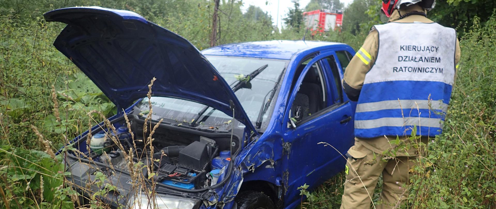 Zdjęcie przedstawia pojazd Skoda Fabia bo kolizji i uszkodzonym przodem oraz lewym bokiem wraz z kierującym działaniem ratowniczym