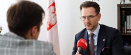 Minister rozwoju i technologii Waldemar Buda udzielający wywiadu radiowego podczas wizyty w Bratysławie, minister mówi do mikrofonu, który trzyma dziennikarz