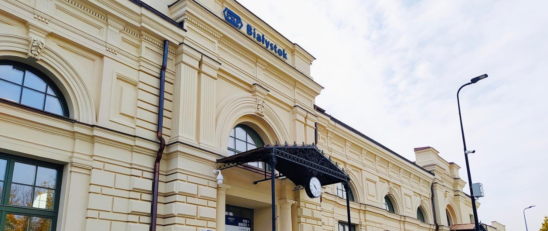 Odnowiony budynek dworca w Białymstoku. Widoczny napis Białystok oraz logo PKP. Poniżej fragment drzwi wejściowych z zadaszeniem i zegarem