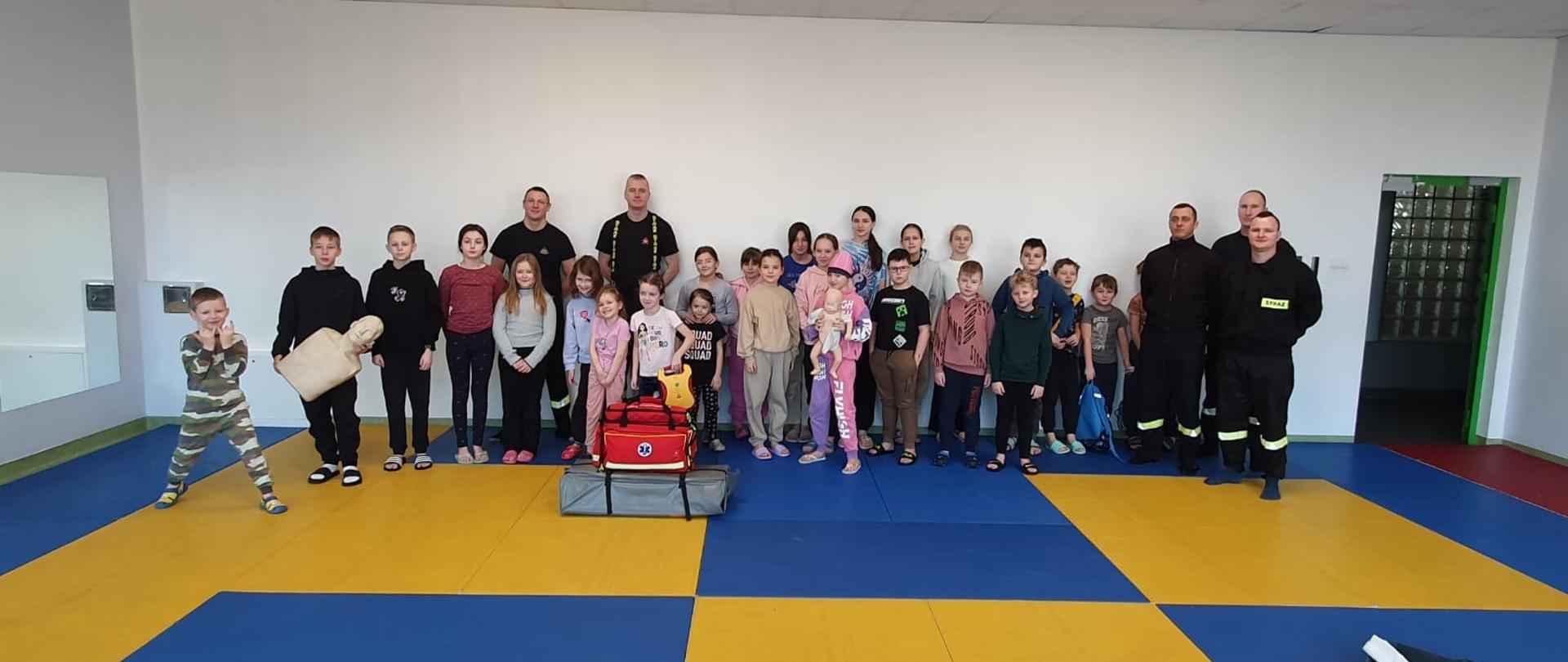 Na zdjęciu w pomieszczeniu grupa dzieci ze strażakami.