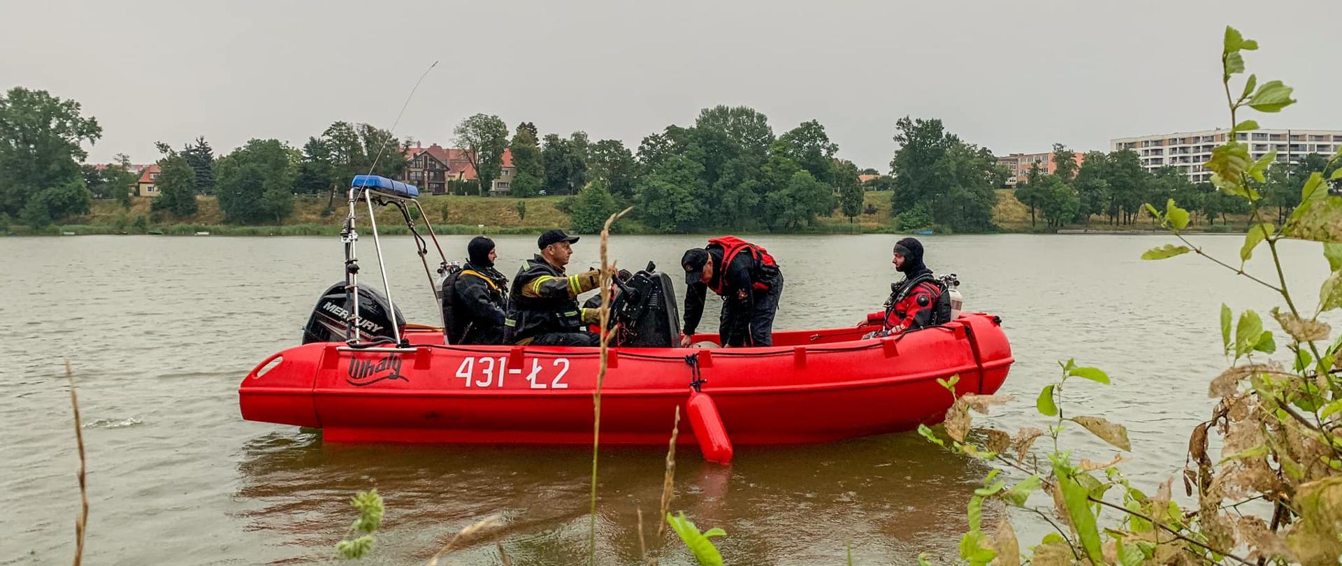 Zdjęcie przedstawia łódź ratowniczą na wodzie a na niej czterech strażaków w tym dwóch nurków ubranych w sprzęt nurkowy