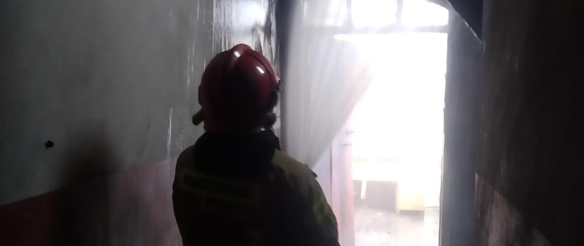 stojący na klatce schodowej strażak podaje prąd wody na palącą się ścianę