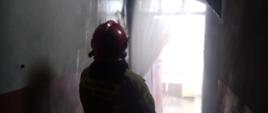 stojący na klatce schodowej strażak podaje prąd wody na palącą się ścianę