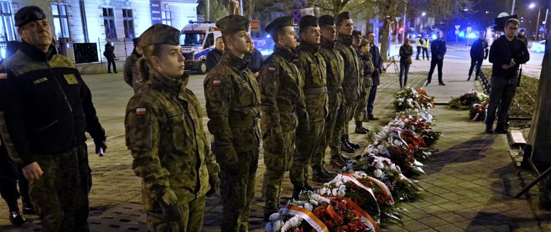 harcerze stoją w szeregu, przed nimi leżą wieńce biało czerwone 