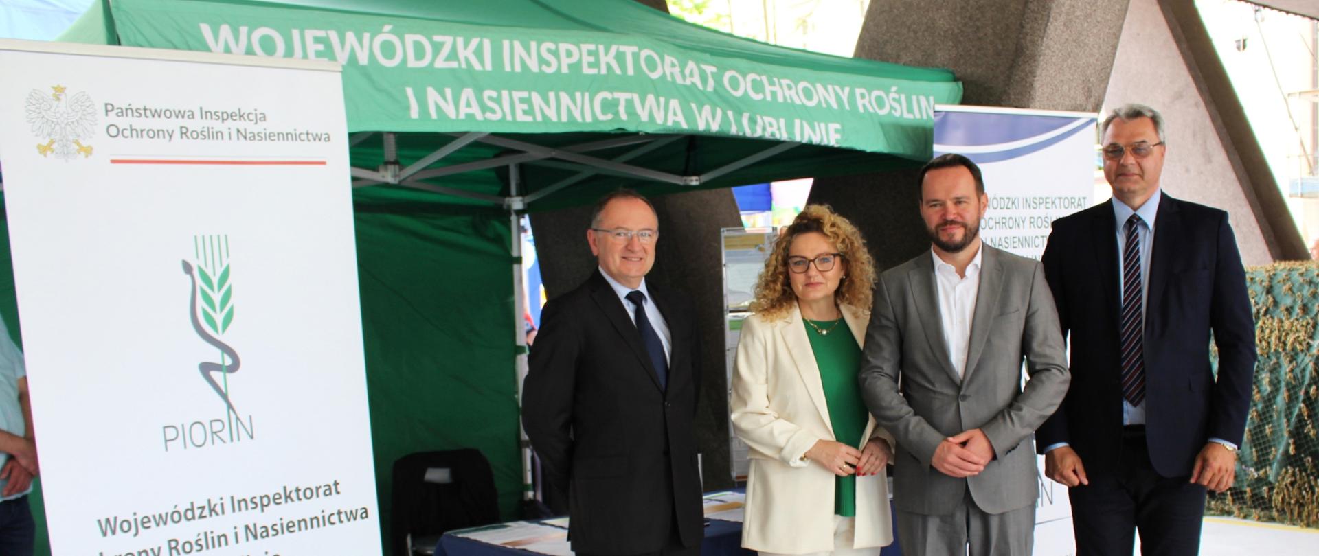 Trzech mężczyzn i kobieta stoją pod namiotem Wojewódzkiego Inspektoratu Ochrony Roślin i Nasiennictwa w Lublinie. Obok stoi rolap Inspekcji.