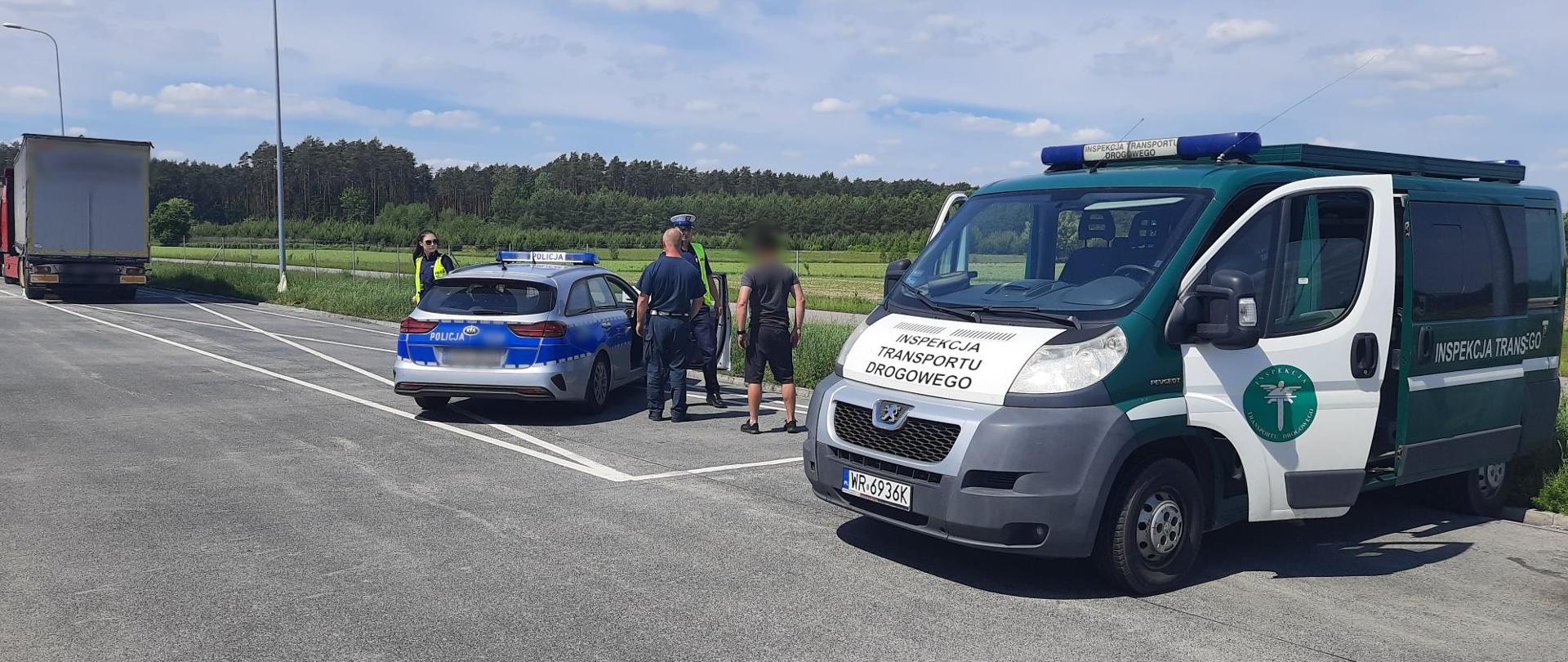 Na pierwszym planie oznakowany radiowóz ITD i Policji. Obok radiowozu Policji stoją policjanci, inspektor ITD i kierowca ciężarówki. W tle zatrzymany zestaw ciężarowy.