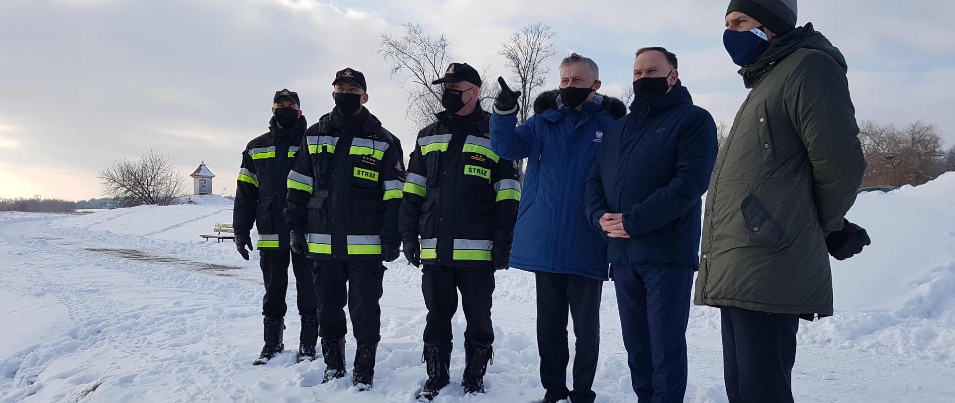 Zdjęcie zrobione na ośnieżonym brzegu rzeki Wisły na bulwarze im. Józefa Piłsudzkiego w Sandomierzu. Na zdjęciu widać Wojewodę Świętokrzyskiego Zbigniewa Koniusza, Posła na Sejm RP Marek Kwitek, dyrektor Zarządu Zlewni Wód Polskich w Sandomierzu Pan Krzysztof Sobecki, Zastępca Świętokrzyskiego Komendanta Wojewódzkiego Państwowej Straży Pożarnej w Kielcach bryg. Grzegorz Rajaca, Komendant Powiatowy Państwowej Straży Pożarnej w Sandomierzu st. kpt. Piotr Krytusa wraz ze swoimi pracownikami. Wojewoda zapoznaje się z aktualną sytuacją hydrologiczną na rzece Wisła i Koprzywianka. 