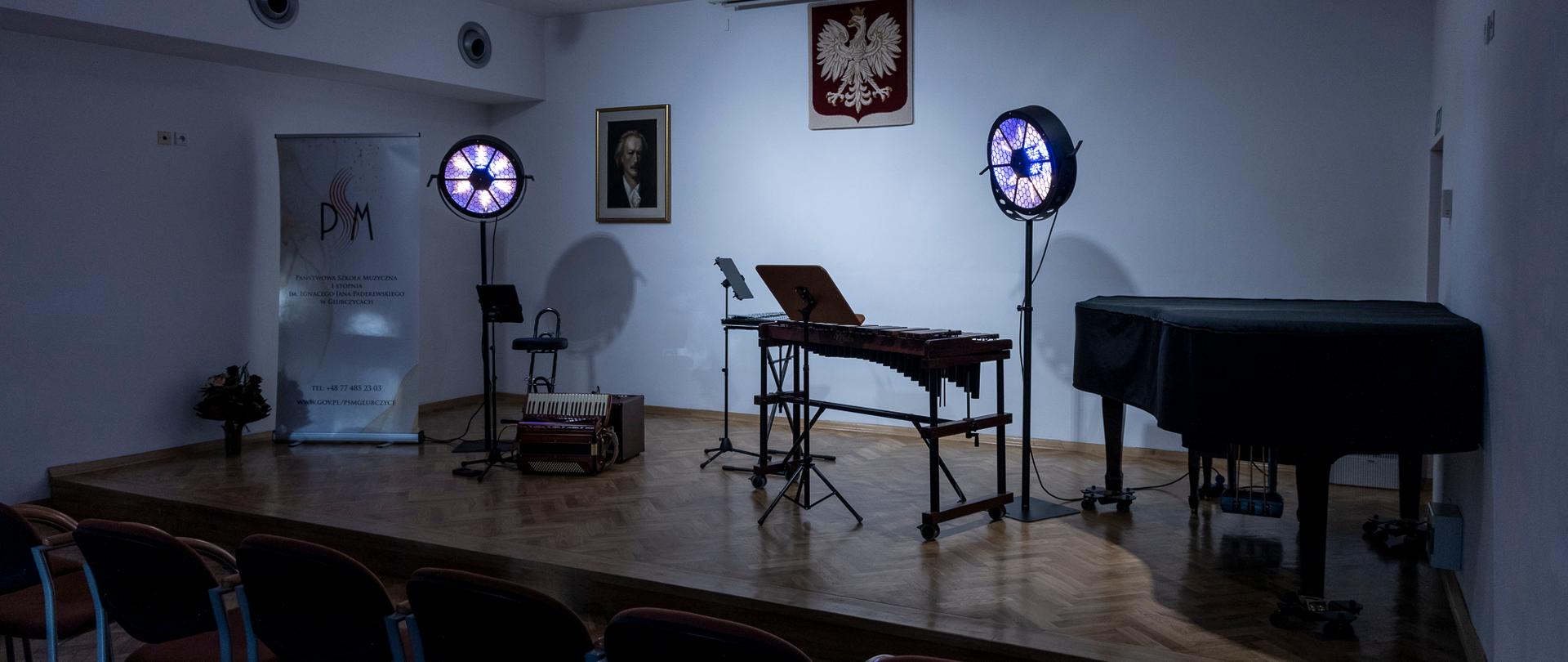 scena auli w państwowej szkole muzycznej w głubczycach, na scenie przygotowane instrumenty - akordeon i ksylofon, widoczne także światła w kształcie koła oraz baner szkoły muzycznej