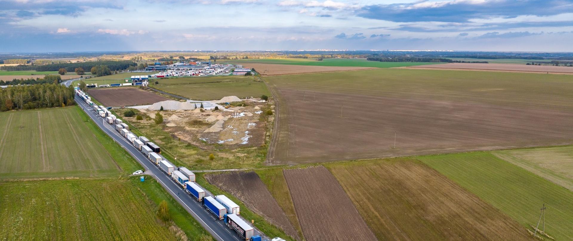 Długa kolejka ciężarówek stojących na jednokierunkowej drodze — pojazdy ustawione są jeden za drugim na kilku kilometrach.