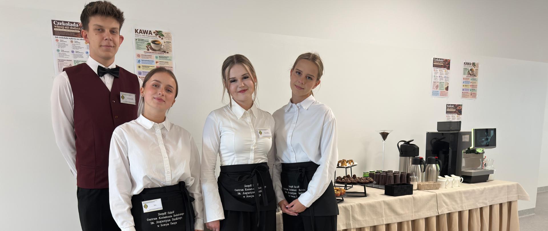 Zdjęcie uczniów Technikum Żywienia i Usług Gastronomicznych przy stołach z kawą i ciastkami