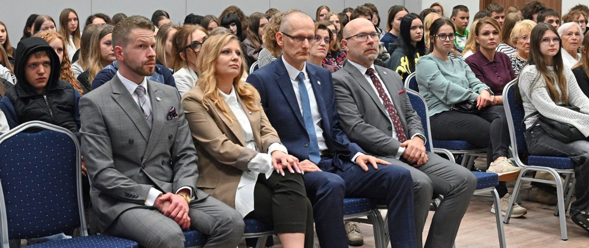 Uczestnicy konferencji „Jesienna profilaktyka kluczem do zdrowia” zorganizowanej przez WSSE w Bydgoszczy. Na pierwszym planie cztery osoby w eleganckich strojach siedzące w pierwszym rzędzie. Za nimi liczna grupa młodzieży i dorosłych uczestników wydarzenia, uważnie słuchających wystąpień. Sala konferencyjna wypełniona jest publicznością.