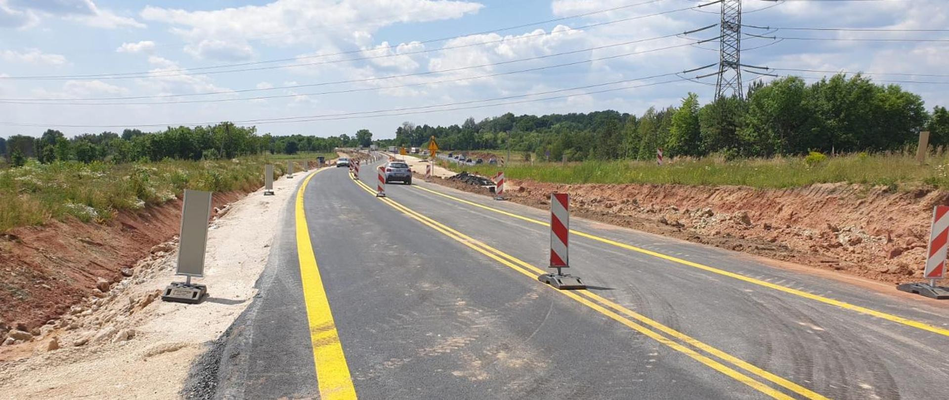 Budowa drogi krajowej DK78. Odcinek Poręba - Zawiercie. Widoczny fragment nowo udostępnionej drogi krajowej z poruszającymi się po niej pojazdami. Na jezdni wymalowane jeszcze żółte oznakowanie tymczasowe oraz rozstawione znaki ostrzegawcze.