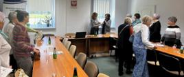 Kobiety stoją przy stole na sali konferencyjnej. Na stole stoją komputer, szklanki, woda w butelkach oraz ciasto i cukierki. W tle baner reklamowy oraz godło Polski