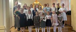 Grupa dzieci pozująca do zdjęcia grupowego wraz z nauczycielem trąbki Wojciechem Lizurejem oraz fletu Bożeną Adamską podczas koncertu klas fletu i trąbki pt. "Wiosenne impresje" - 19 maja 2023