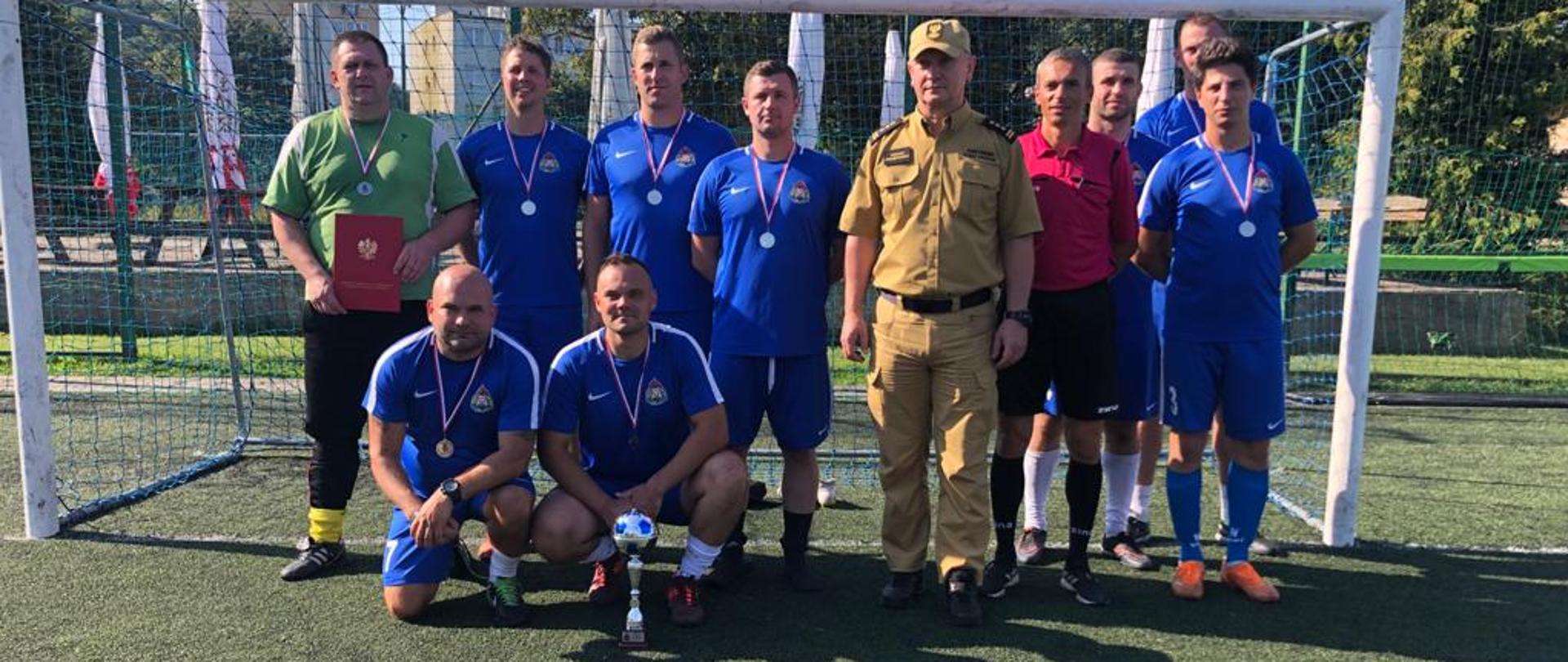 Fotografia przedstawia reprezentację strażaków z Jednostki Ratowniczo Gaśniczej w Malborku ustawionych do zdjęcia po zdobyciu drugiego miejsca na czwartych mistrzostwach województwa pomorskiego w piłce nożnej
