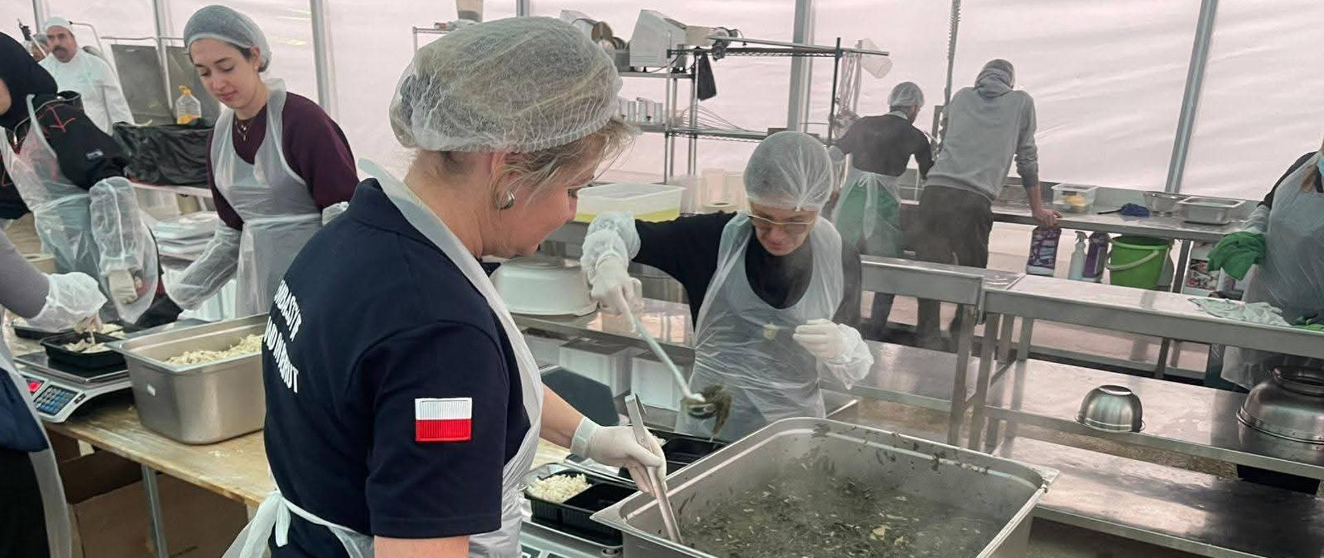 Kobiety w czepkach ochronnych i fartuchach nakładają jedzenie z podgrzewaczy do małych pojemników