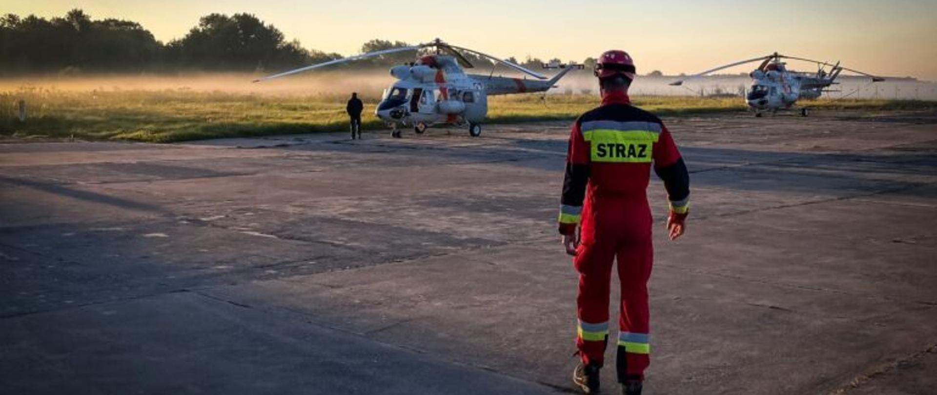 Funkcjonariusz PSP na placu, na którym znajdują się dwa śmigłowce
