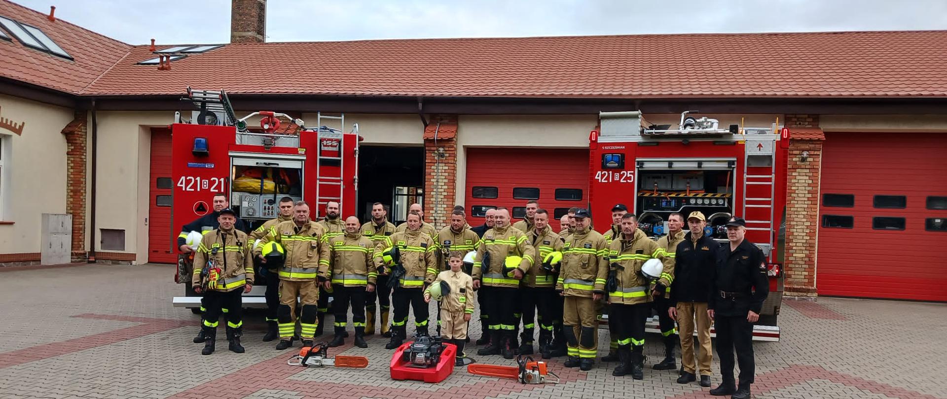 Uczestnicy kursu oraz komisja egzaminacyjna pozują na tle pojazdów pożarniczych