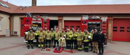 Uczestnicy kursu oraz komisja egzaminacyjna pozują na tle pojazdów pożarniczych