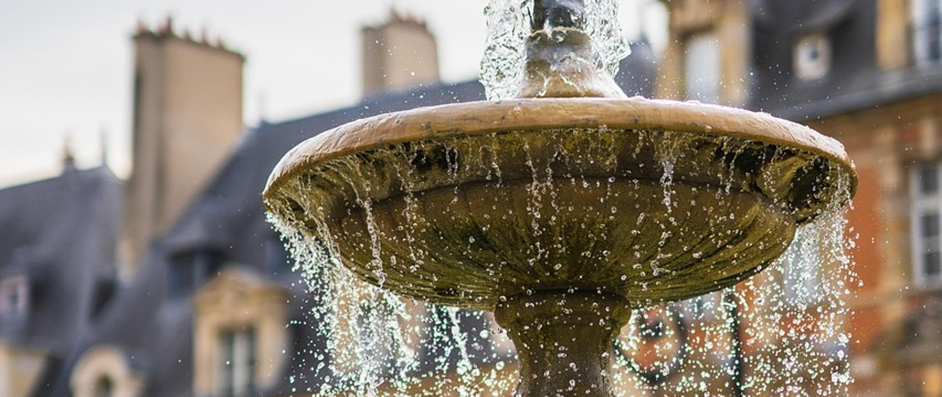 na zdjęciu fontanna w tle budynki
