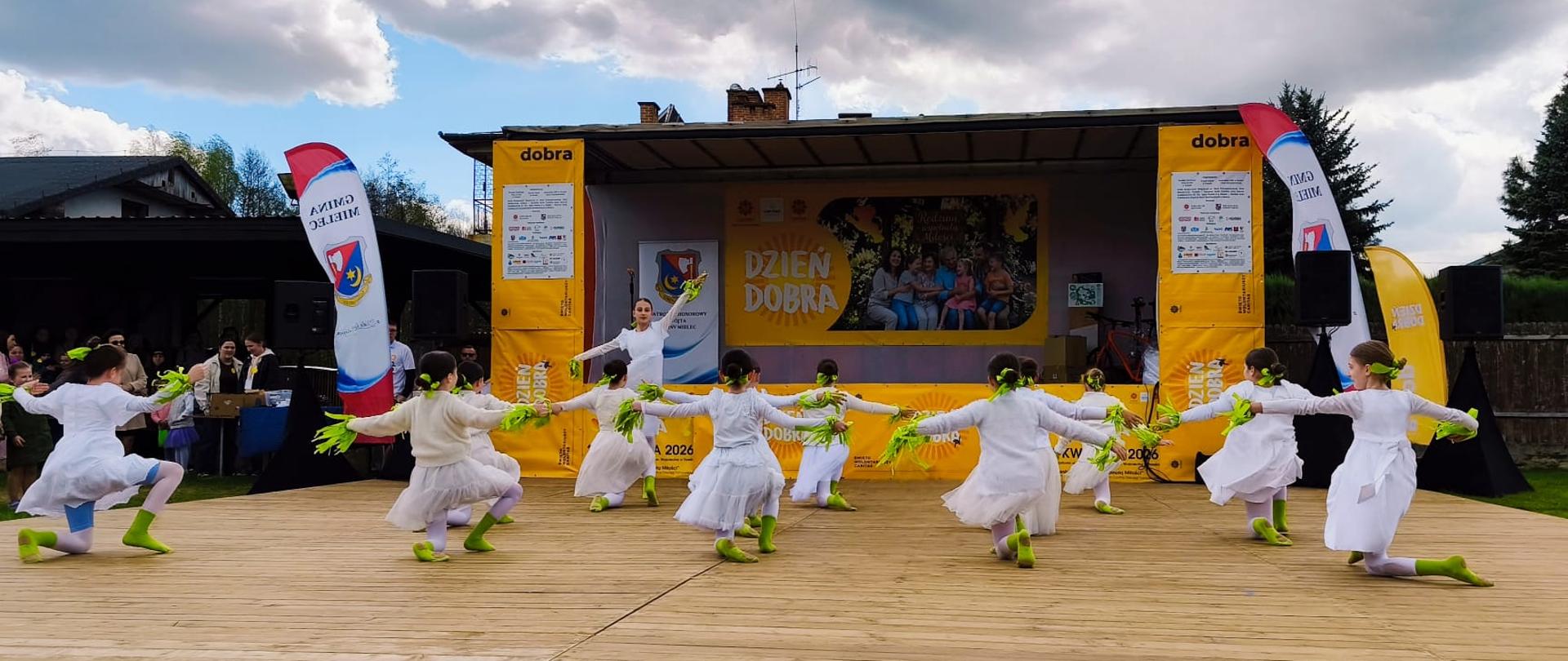 Grupa uczennic w białych strojach wykonująca układ taneczny na scenie plenerowej podczas Ogólnopolskiego Dnia Dobra w Trześni.