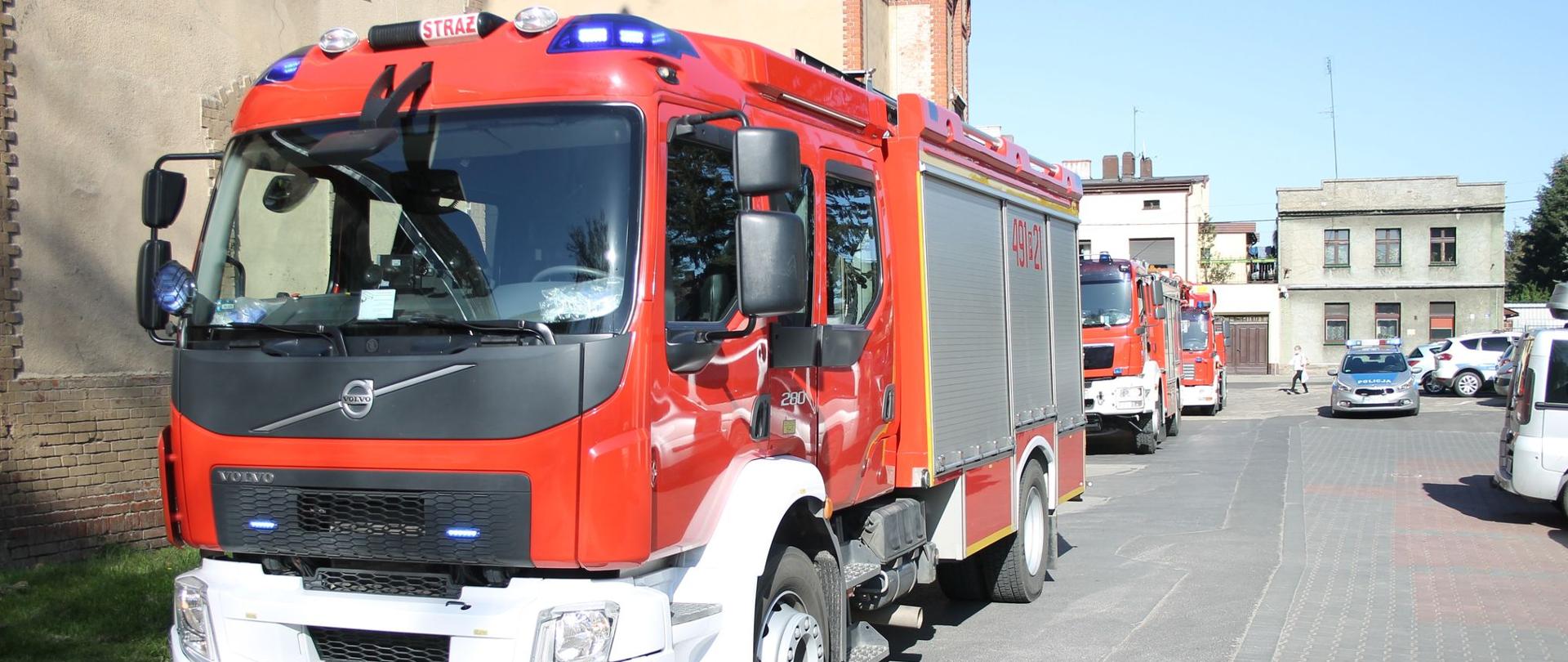 Zdjęcie przedstawia dwa samochody Państwowej Straży Pożarnej stojące obok budynku z cegły.