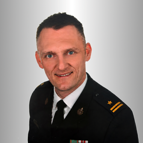 Młodszy brygadier Bartosz Smolarczyk w mundurze wyjściowym na tle gradientu.