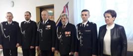 Na zdjęciu stoją na baczność w rzędzie druhowie OSP Doły Biskupie oraz przedstawiciel Urzędu Miasta i Gminy Kunów po ceremonii wręczenia odznaczeń OSP. Zdjęcie wykonane w remizie OSP Doły Biskupie.