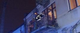 Strażak na balkonie pierwszego pietra w mieszkaniu w którym doszło do pożaru wyposażony w aparat ochrony dróg oddechowych. 