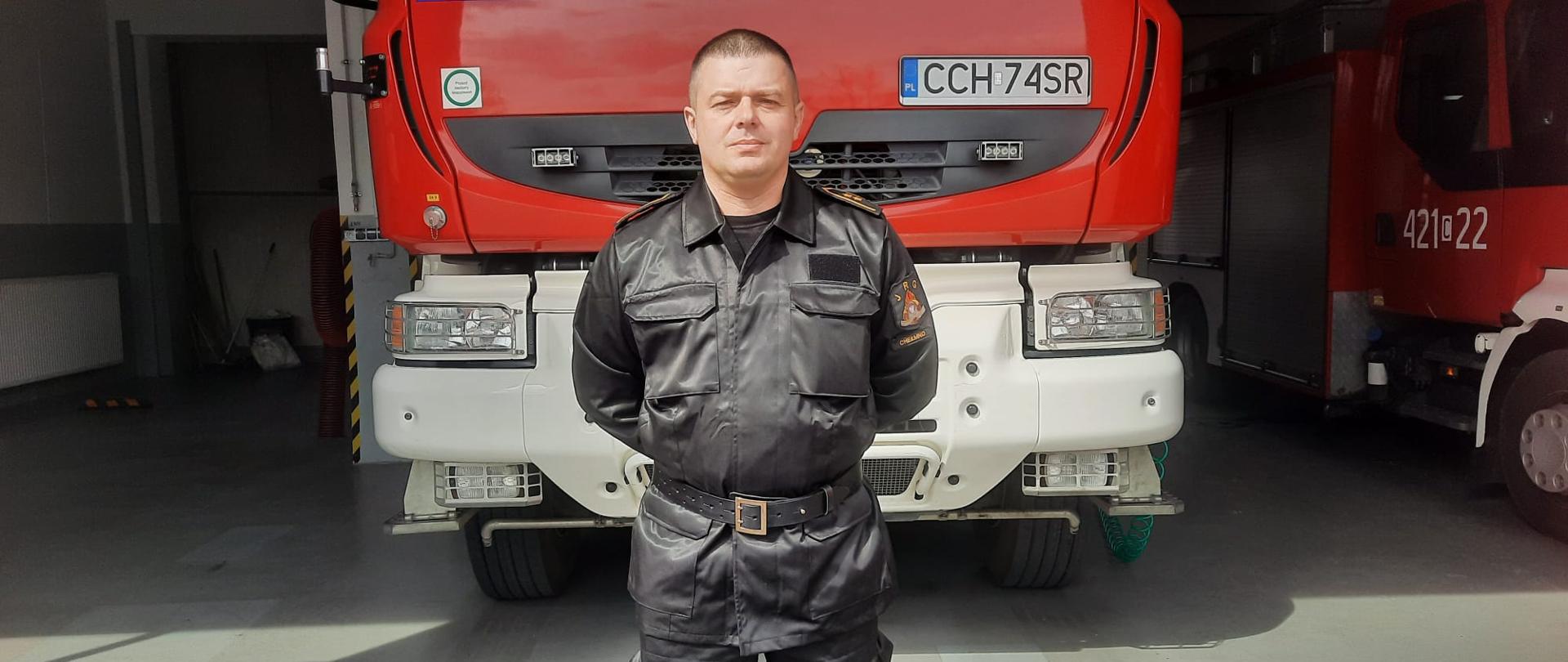 Na tle samochodu gaśniczego stoi zastępca dowódcy JRG