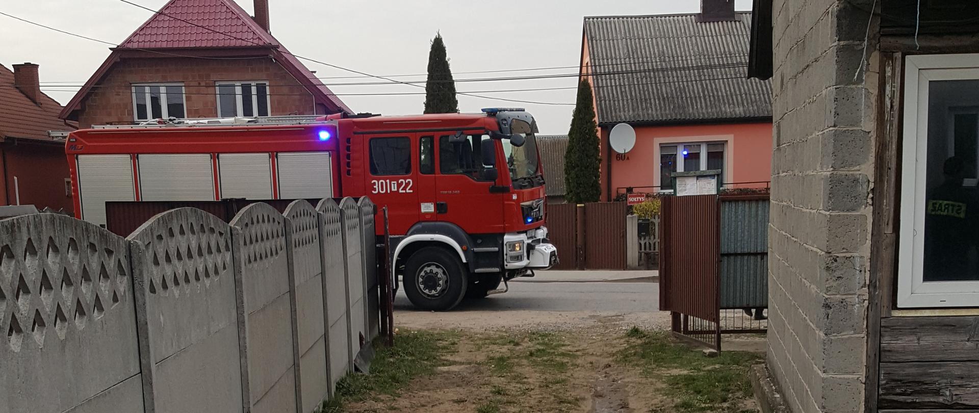 Zdjęcie przedstawia wjazd na posesję - w oddali na ulicy widać samochód straży pożarnej.
