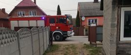 Zdjęcie przedstawia wjazd na posesję - w oddali na ulicy widać samochód straży pożarnej.