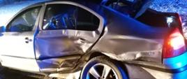 Na zdjęciu samochód osobowy po wypadku. Na zdjęciu widoczne uszkodzone tylne drzwi z lewej strony pojazdu oraz uszkodzony tylni lewy bok pojazdu, otwarty bagażnik. 