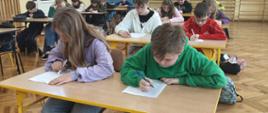 Na zdjęciu widoczne są dzieci siedzące w ławkach, w trakcie pisania testu.