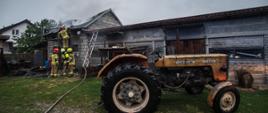 Na zdjęciu na drugim planie widocznych pięciu strażaków dogaszających budynek gospodarczy. Na pierwszym planie traktor marki Ursus.
