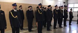 Część wyróżnionych strażaków stojąca w pododdziale w ubraniach wyjściowych. Na głowach czapki rogatywki, berety, Panie mają kapelusze, wszyscy maski na twarzach