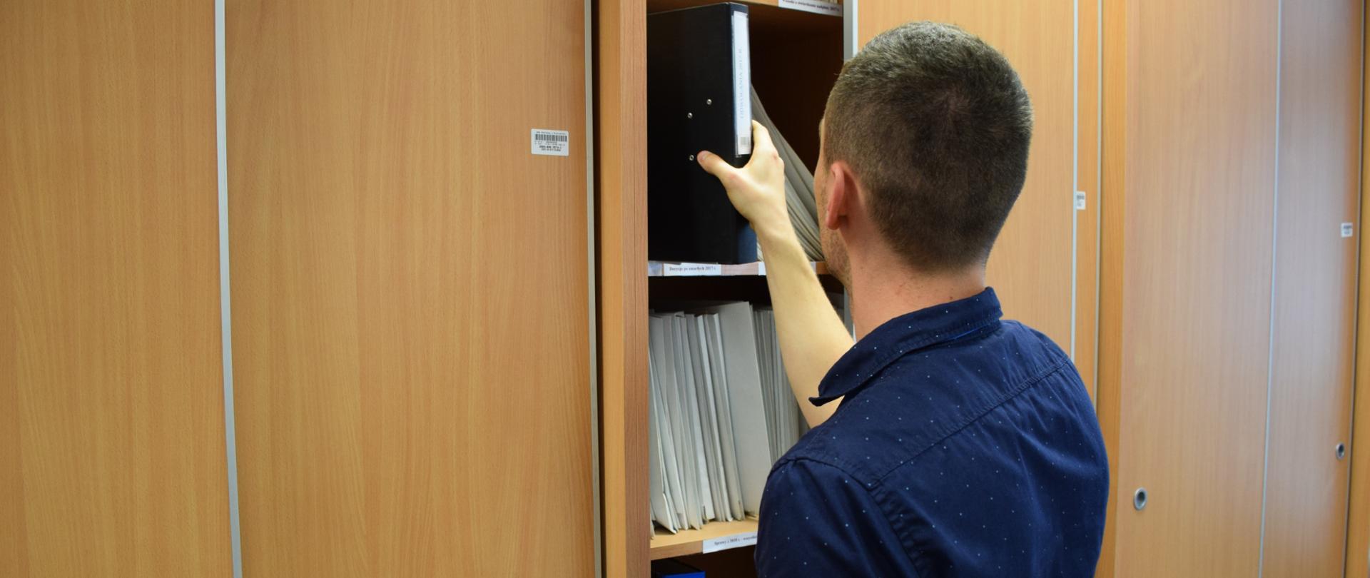 Pracownik urzędu skarbowego wyjmuje dokumenty z szafy