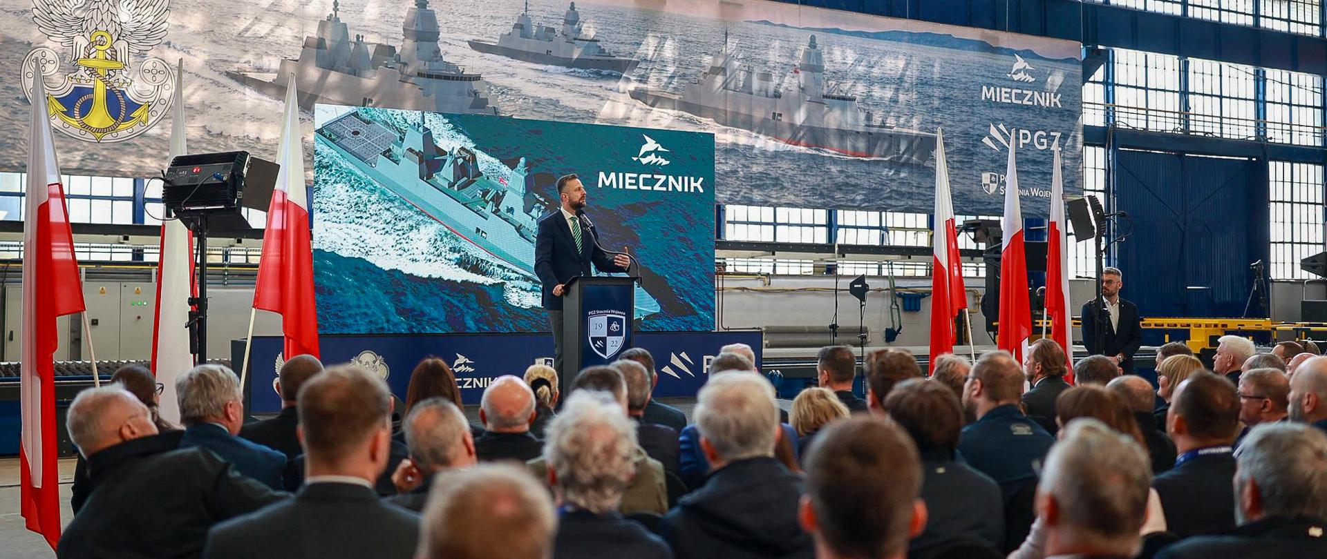 sala, dużo osób w tle ktoś przemawia