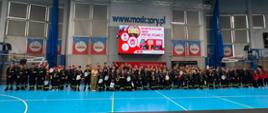 
Uczestnicy II Halowych Młodzieżowych Zawodów Sportowo-Pożarniczych pozują do wspólnego zdjęcia na hali sportowej MOSiR w Żorach, trzymając dyplomy i medale.

